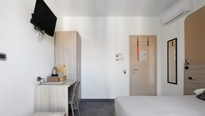 Una camera d'albergo con un letto, una scrivania con una sedia, un televisore a parete e una porta con maniglia.