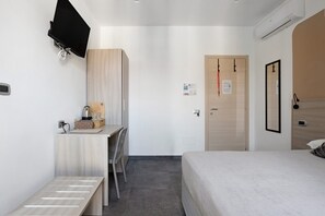 A hotel room with a bed, a desk with a chair, a television mounted on the wall, and a door with a handle. - Room - Rosmarino with Balcony, Wi-Fi and Air Conditioning (La Spezia)