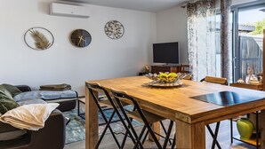 Ett modernt vardagsrum med ett matbord i trä, svarta stolar, en soffa, en tv och dekorativ väggkonst.