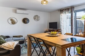 A modern living room with a wooden dining table, black chairs, a sofa, a TV, and decorative wall art. - L'Océan - Au calme de la Campagne (Saint-Martin-de-Hinx)