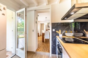 Une cuisine moderne avec un revêtement mural en marbre noir, des appareils en acier inoxydable et un coin repas visible à travers une porte ouverte.
