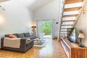 Un salon avec un canapé, une table basse, un téléviseur et un escalier.