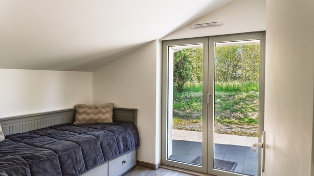 Une chambre avec un lit, une porte-fenêtre coulissante donnant sur un espace extérieur et une petite fenêtre.
