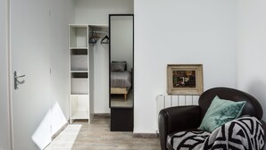 Une chambre à coucher comprenant une armoire, un lit, une chaise avec un plaid et un tableau encadré accroché au mur.