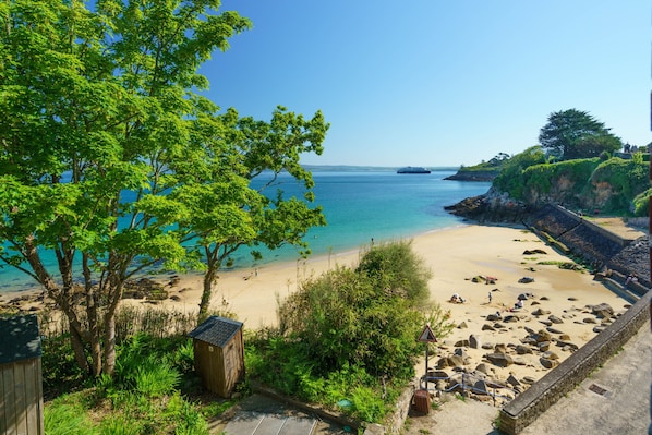 Une plage à l’eau d’un bleu limpide, avec un rivage sablonneux et une petite construction en bois.