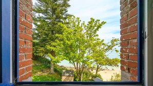 Blick durch ein Fenster auf eine Ziegelmauer und einen Baum im Vordergrund, der zu einem Strand führt.