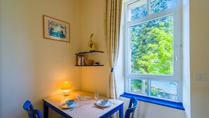 Ein Essbereich mit Tisch für zwei Personen, einer Lampe und einem Fenster mit Blick auf Bäume.