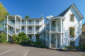 Un immeuble à plusieurs étages doté de balcons, d’un parking et entouré de verdure.