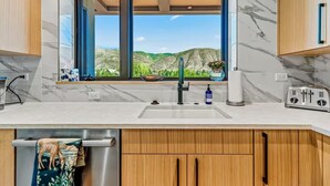 Una cocina moderna con un amplio ventanal, un lavamanos de acero inoxidable y armarios de madera.