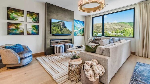 Un salón moderno con chimenea, un televisor grande y un sofá con vistas al exterior.