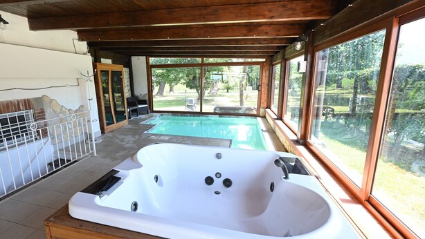 Un área de spa con jacuzzi, terraza de madera y grandes ventanales con vistas a un jardín.