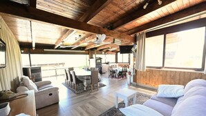 Un amplio espacio de estar con techo de madera, una mesa de comedor con sillas y un sofá.