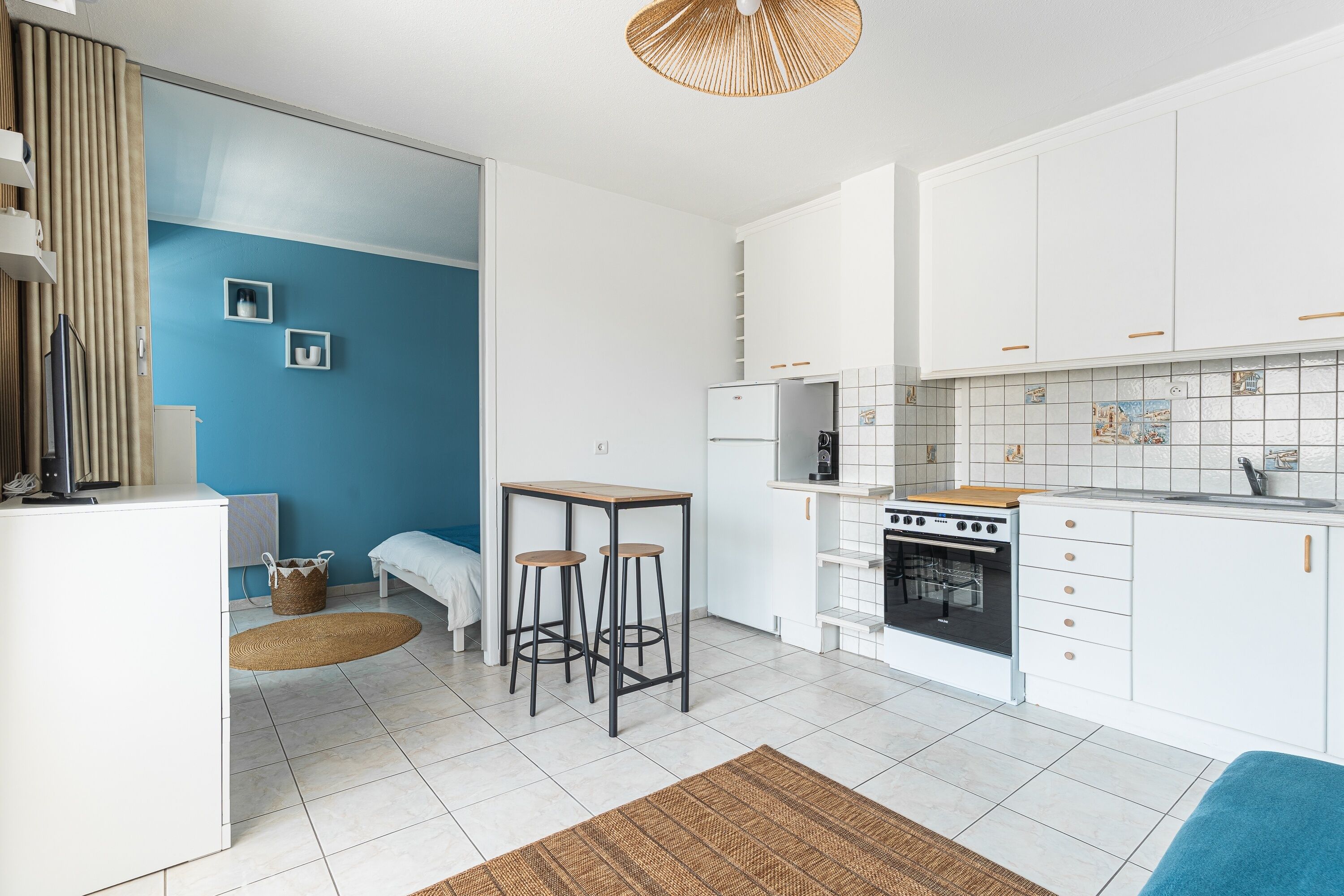 A compact kitchen with white cabinets, a stove, and a small dining area with stools.