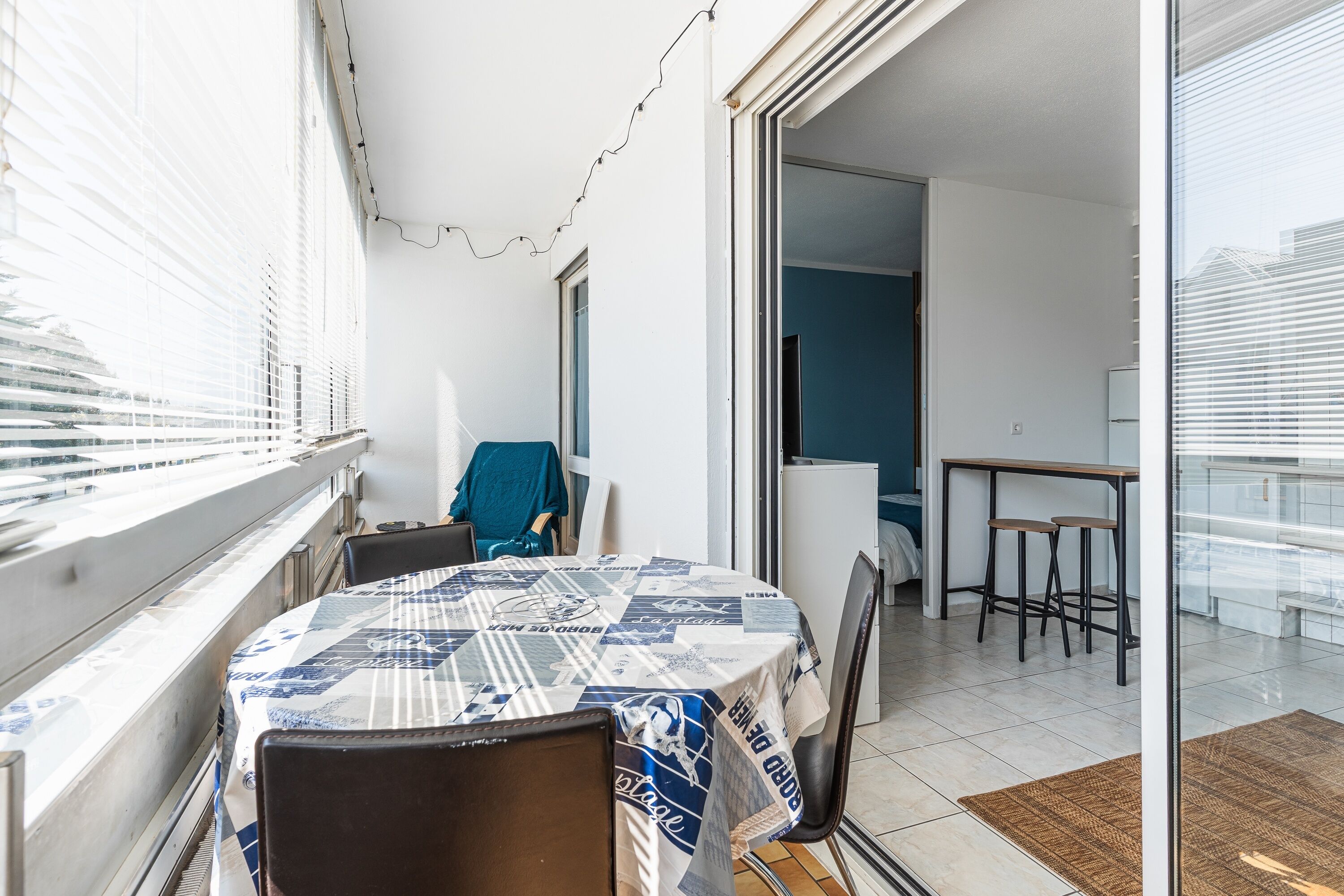 A balcony with a table covered in a patterned tablecloth, chairs, and a view of the city.