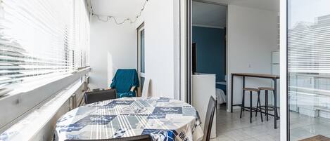 A balcony with a table covered in a patterned tablecloth, chairs, and a view of the city.