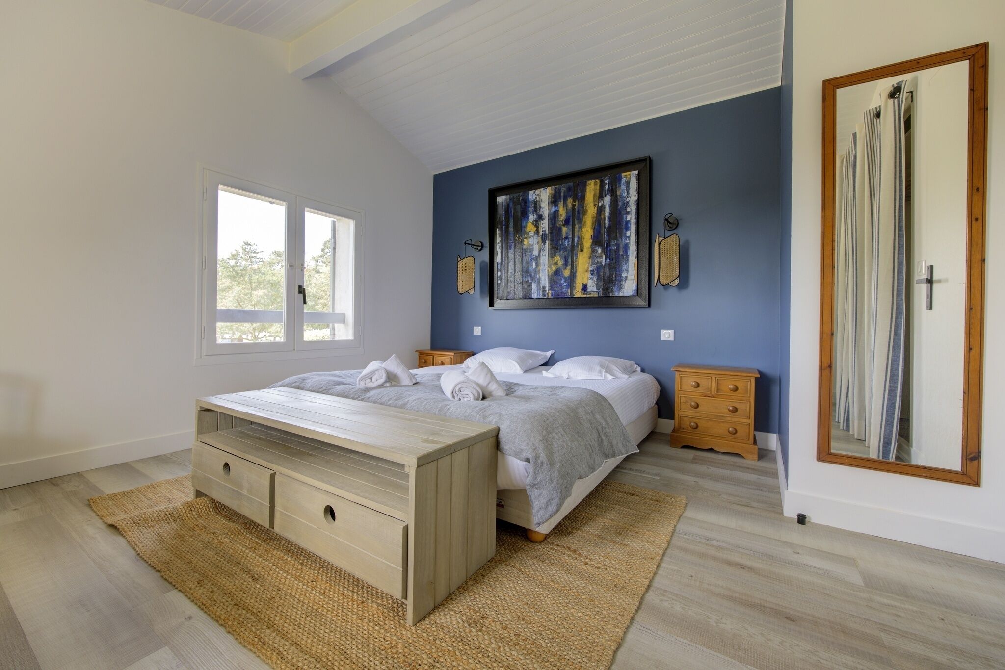 Ein Schlafzimmer mit einem Bett, einer hölzernen Bank, einem Schminktisch und einem großen Gemälde sowie einem Spiegel.