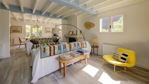 A room with a bed, a yellow armchair, a wooden table, and a window with curtains. - Villa Veronica - À 50 m de la plage (Lège-Cap-Ferret)
