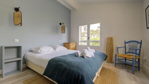 A bedroom with a bed, a chair, a window, and a wall-mounted light fixture. - Villa Veronica - À 50 m de la plage (Lège-Cap-Ferret)