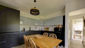 A modern kitchen with dark cabinets, a wooden dining table, and a hanging light fixture. - Villa Veronica - À 50 m de la plage (Lège-Cap-Ferret)