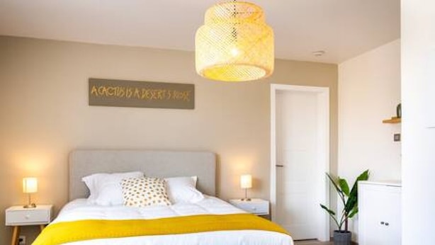 Un dormitorio con cama, mesitas de noche, una lámpara colgante, una puerta y un cartel en la pared.