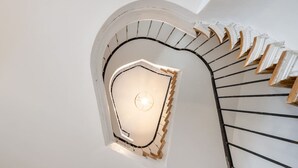 Una escalera de caracol junto a una pared blanca y una lámpara en la parte superior.