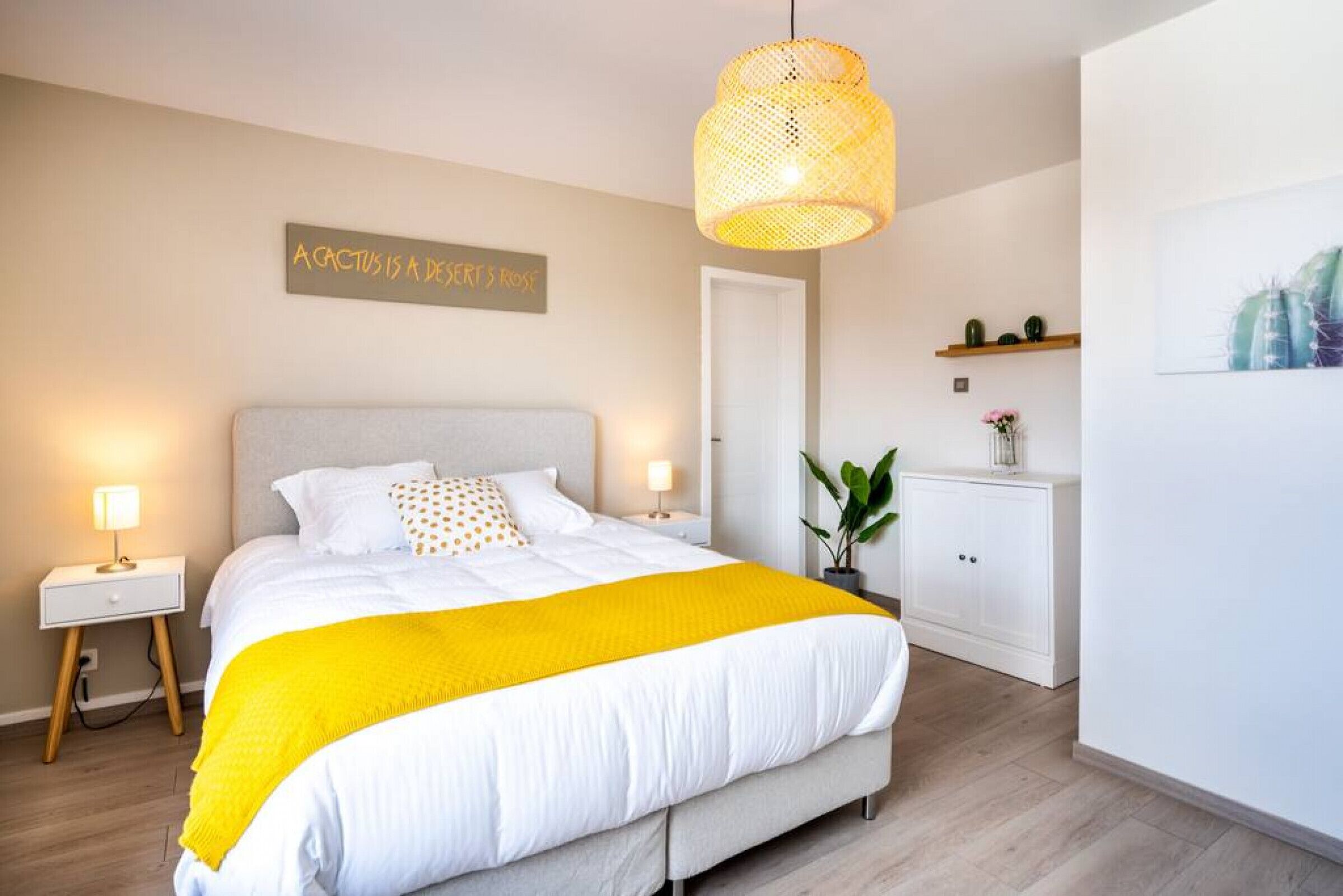 A bedroom with a bed, bedside lamps, a hanging light fixture, a door, a cabinet, and a wall-mounted sign.
