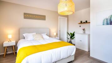 A bedroom with a bed, bedside lamps, a hanging light fixture, a door, a cabinet, and a wall-mounted sign.