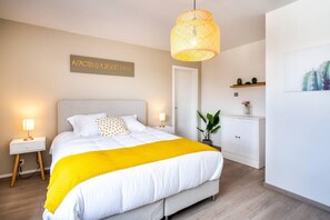 Une chambre à coucher comprenant un lit, des lampes de chevet, un luminaire suspendu, une porte, une armoire et un panneau fixé au mur.