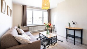 Una sala moderna con un sofá, una mesa de centro, un tapete estampado con diseño de cebra, una lámpara de pie y vistas al exterior a través de amplios ventanales.