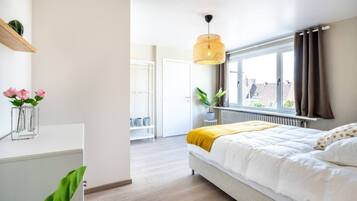 Ein Schlafzimmer mit Bett, einem Fenster mit Vorhängen, einem Nachttisch mit Pflanze und einer Hängelampe.