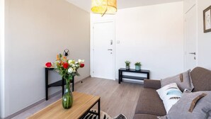 Una sala de estar moderna con un sofá, una mesa de centro de madera, un florero con flores, una lámpara colgante y una puerta al fondo.