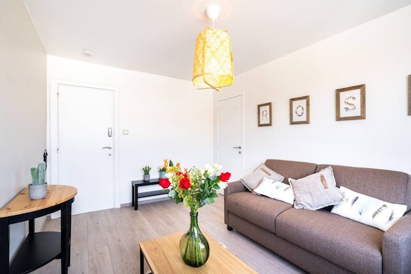 Un salon moderne avec un canapé, une table basse, un vase de fleurs, un luminaire suspendu et des tableaux encadrés au mur.
