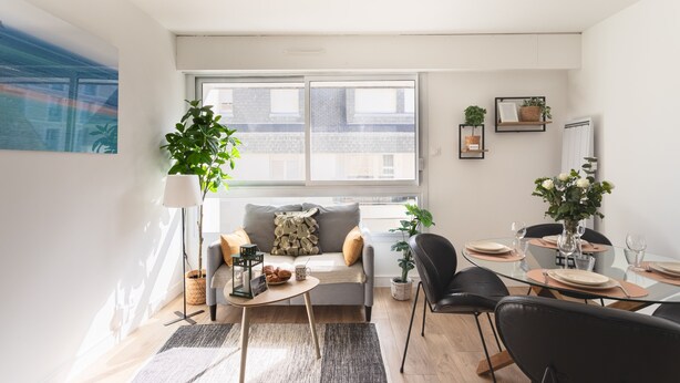 A modern living room with a sofa, coffee table, and dining area. - Le Winston - Bel appartement proche de la plage (Dinard)