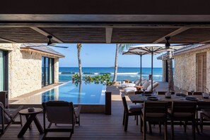Un espace aménagé au bord de la piscine, avec vue sur l’océan, des sièges extérieurs et un espace de restauration couvert.