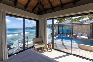 Une chambre avec une grande fenêtre donnant sur une piscine et l’océan.