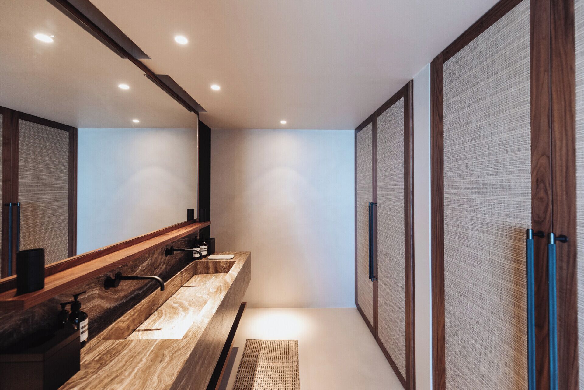 Ein modernes Badezimmer mit einem Holzwaschtisch, einem großen Spiegel und einer Wandverkleidung mit Struktur.