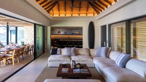 A modern living room with a wooden ceiling, a large sofa, a coffee table, and a dining area with a view.