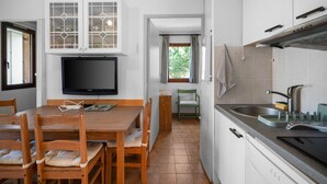 Cozinha compacta com área de refeições, televisão e janela com cortinas.
