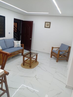 A living room with a sofa, two wooden chairs, a glass coffee table, a dark wooden door, and a framed picture on the wall. - Sunrise Ocean Views Rooftop with BBQ Near SDQ (Santo Domingo Este)