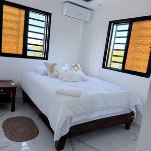 A bedroom with a bed, pillows, a bedside table, an air conditioning unit, and a window with a view. - Sunrise Ocean Views Rooftop with BBQ Near SDQ (Santo Domingo Este)