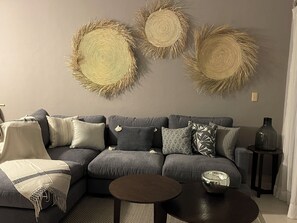 Ein Wohnzimmer mit grauem Sofa, mehreren Kissen, einem runden Couchtisch und Wanddekoration.