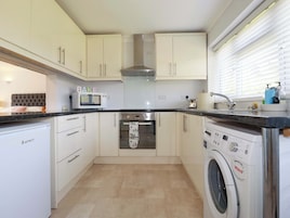 A compact kitchen with a microwave, oven, washing machine, and a sink.