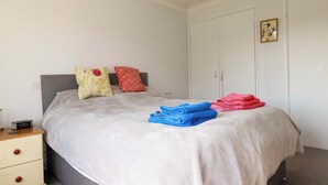 Una cama bien tendida con almohadas, una mesita de noche con lámpara y un armario en una habitación con paredes blancas.