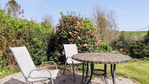 Una mesa redonda con dos sillas, rodeada por un jardín con un arbusto de flores rosas.