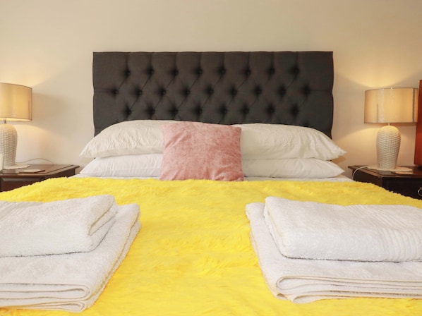 Habitación de hotel con cabecera acolchada, colcha amarilla brillante, almohadas blancas y rosas, y dos lámparas de noche.