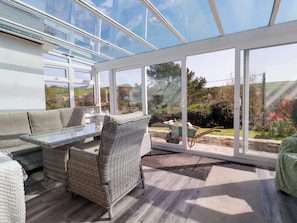 Un solárium con techo de cristal, muebles de mimbre y vistas al exterior.