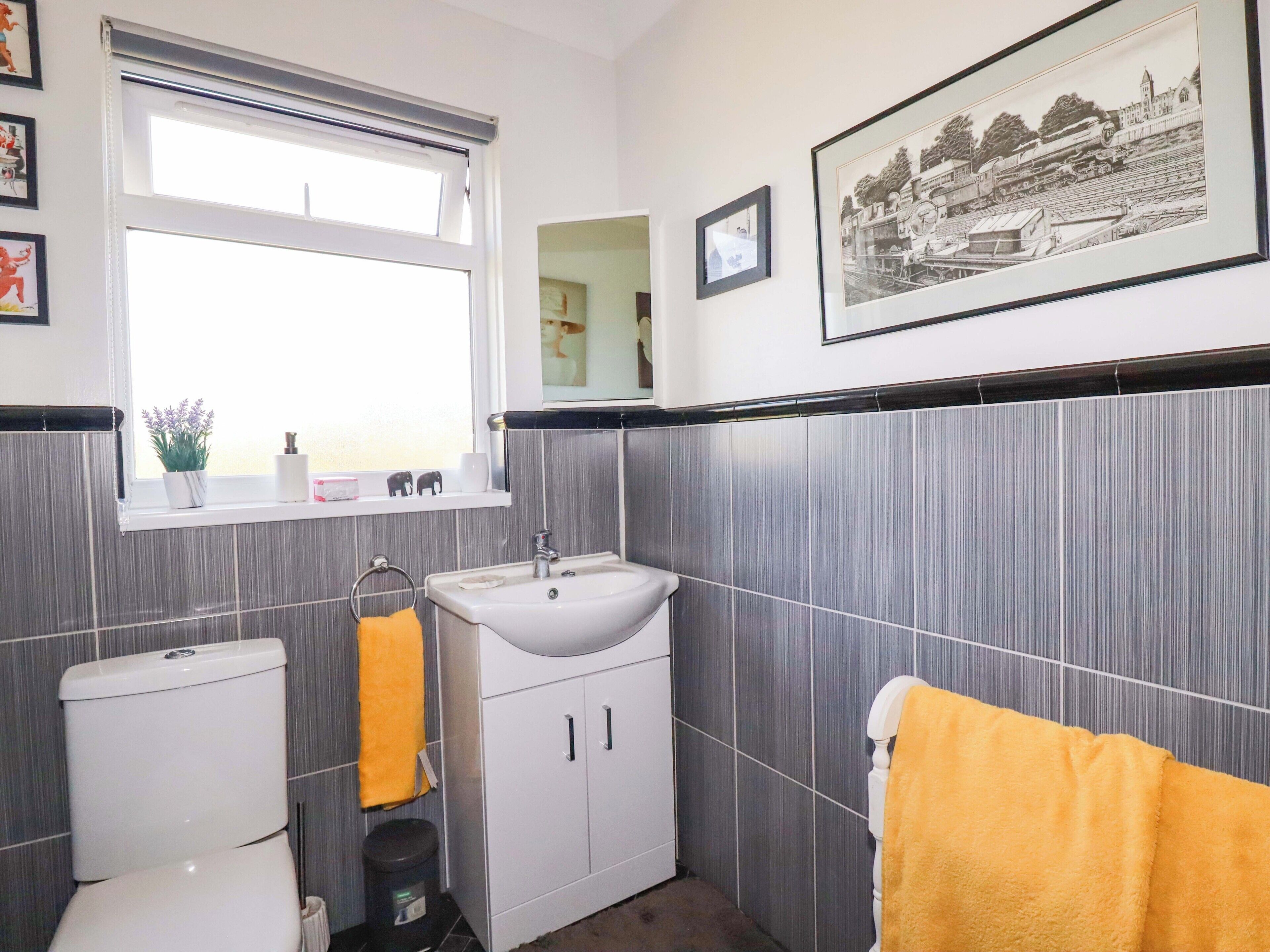 Une salle de bain comprenant des toilettes, un lavabo et un miroir, avec une fenêtre et des tableaux encadrés accrochés au mur.