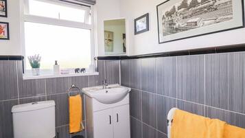 Une salle de bain comprenant des toilettes, un lavabo et un miroir, avec une fenêtre et des tableaux encadrés accrochés au mur.