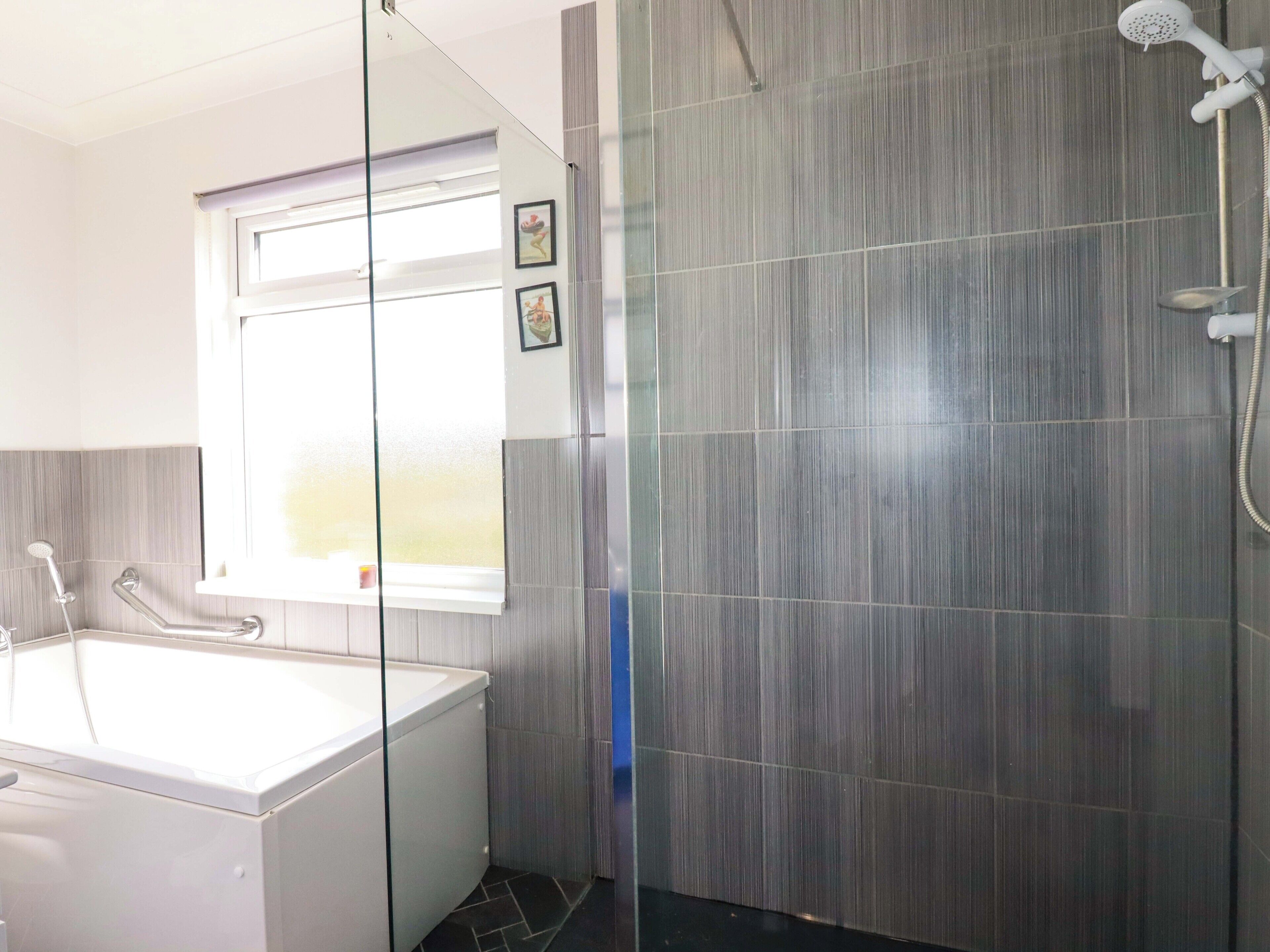A modern bathroom with a bathtub, a glass shower enclosure, and a window with a picture.