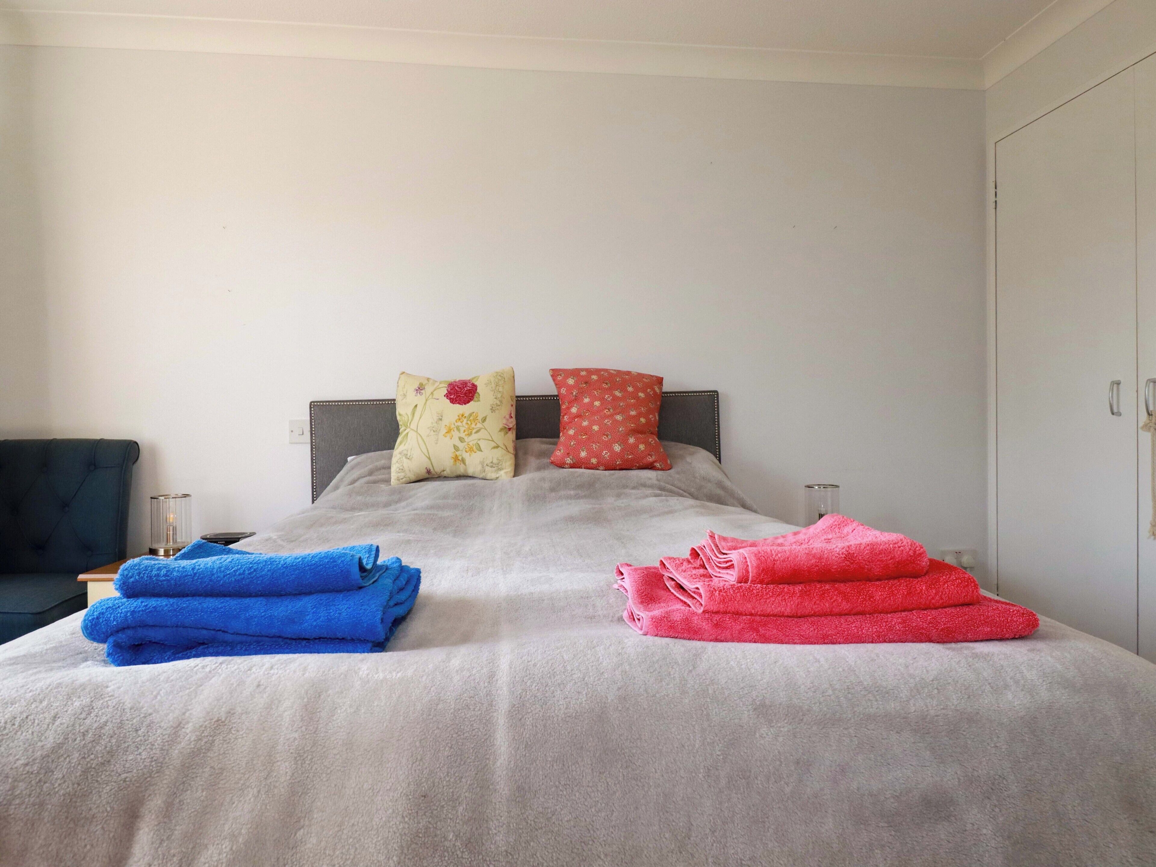 Una cama con edredón gris, dos almohadas y dos toallas dobladas.